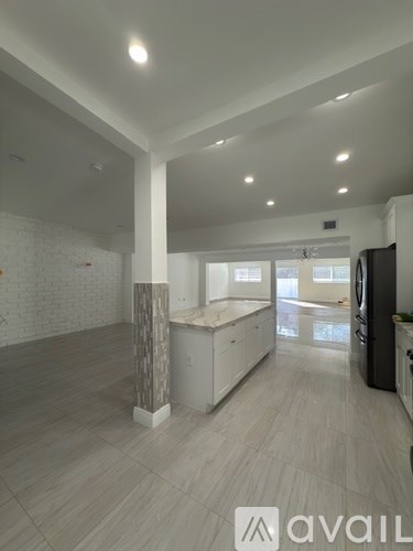 A spacious kitchen with white cabinets and a black refrigerator.