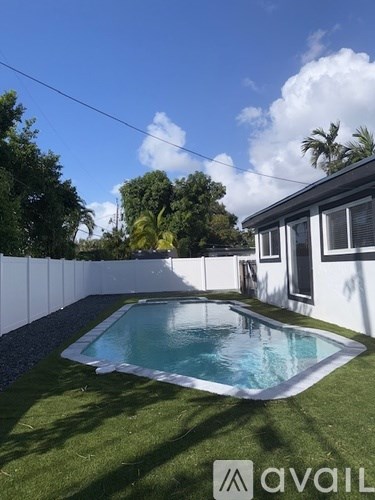 A pool in a backyard with a white fence and a house in the background.