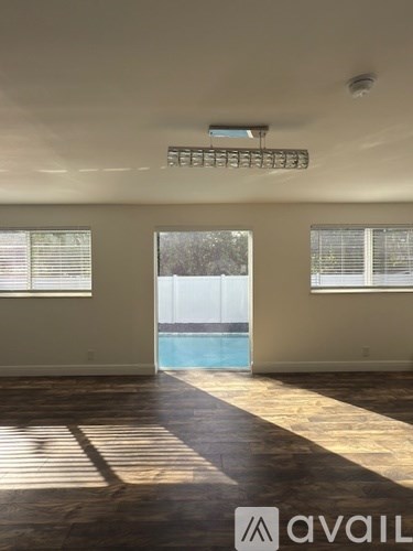 A room with wooden floors and a pool visible through the window.