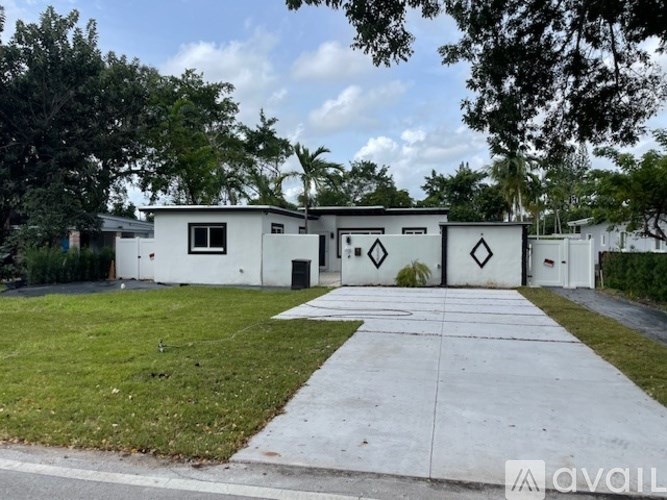 A white building with a black door and windows is surrounded by greenery.