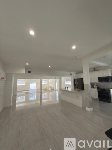 A spacious living room with a television and a kitchen area in the background.
