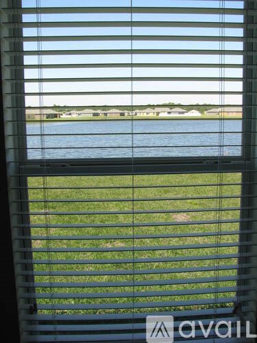 A view of a lake through a window with blinds.