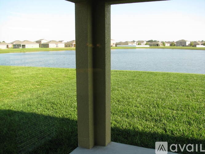 A grassy field with a body of water and houses in the background.