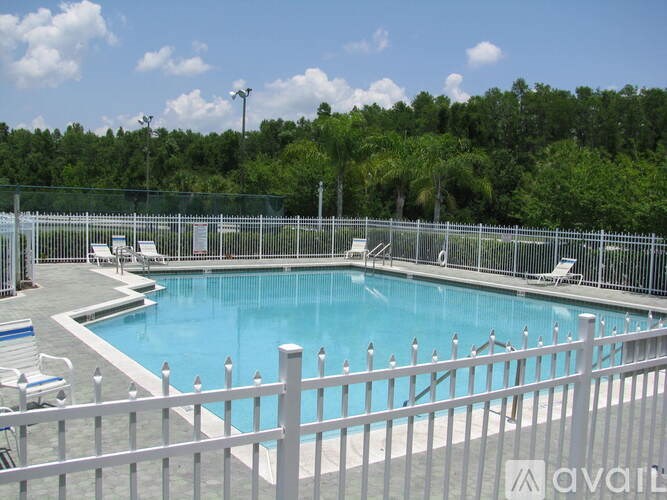 A pool surrounded by a white fence with chairs around it.