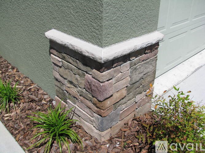 A grey house with a white door and a stone pillar in front of it.