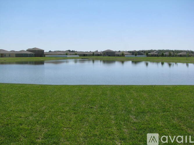 A grassy field with a lake and houses in the background.