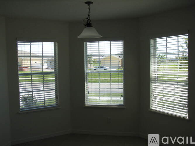 Three windows with blinds in a room with a hanging light fixture.
