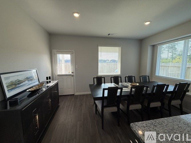 A living room with a television, a dining table and chairs, and a large window.