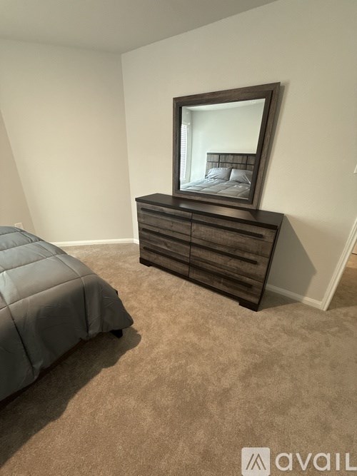 A bedroom with a grey bedspread and a brown dresser with a mirror on top.