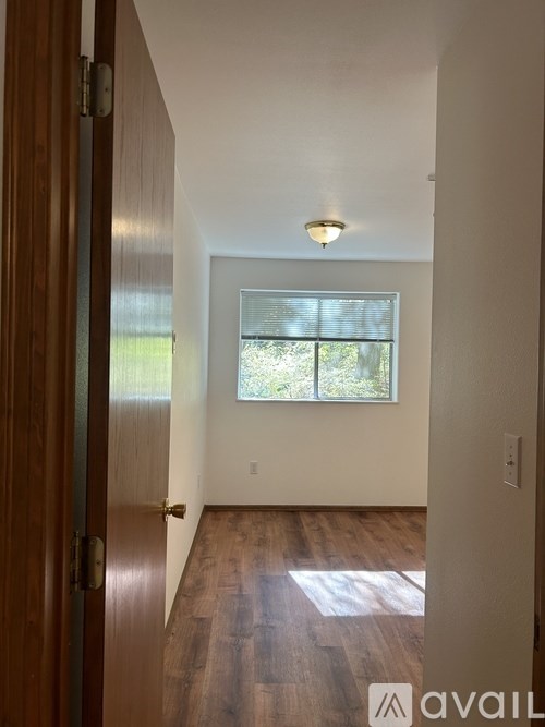 A hallway with a wooden floor and a window with blinds.