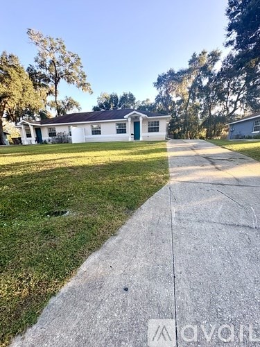 A white house with a green door is situated on a street with a sidewalk.