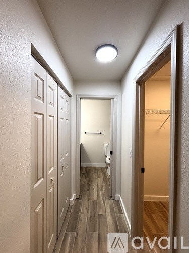 A hallway with wooden floors and white walls leading to a bathroom.