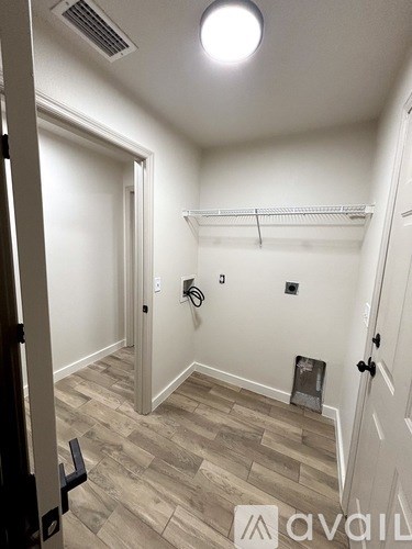 A room with a wooden floor and a white wall with a shelf and a light fixture.