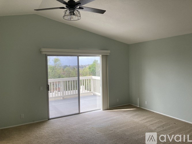 A room with a ceiling fan and sliding glass doors leading to a balcony.