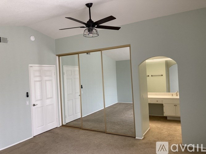 A bedroom with a mirrored closet door and a ceiling fan.