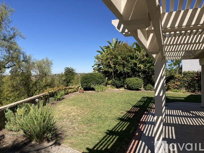 A patio with a white pergola and a view of a green lawn and trees.