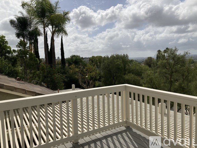 A balcony with a white railing overlooks a landscape with trees.