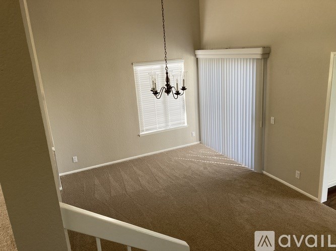 A room with a carpeted floor, a window with blinds, and a chandelier hanging from the ceiling.