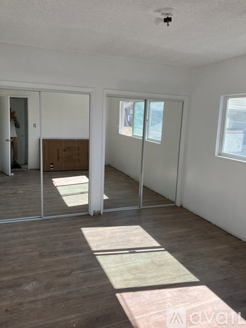 A room with white walls and wooden flooring, with a door on the left and a window on the right.