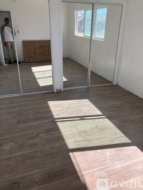 A man is standing in a room with a wooden floor and white walls.