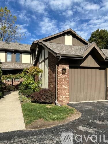 A house with a brown garage door is surrounded by greenery.