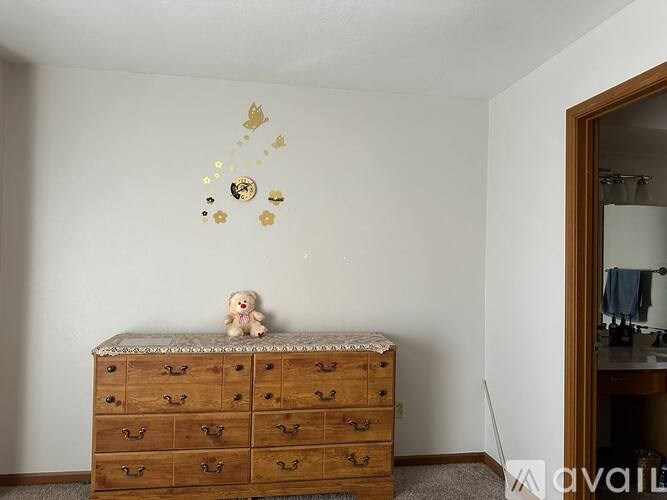 A white wall with a teddy bear on a bed and a dresser with drawers.