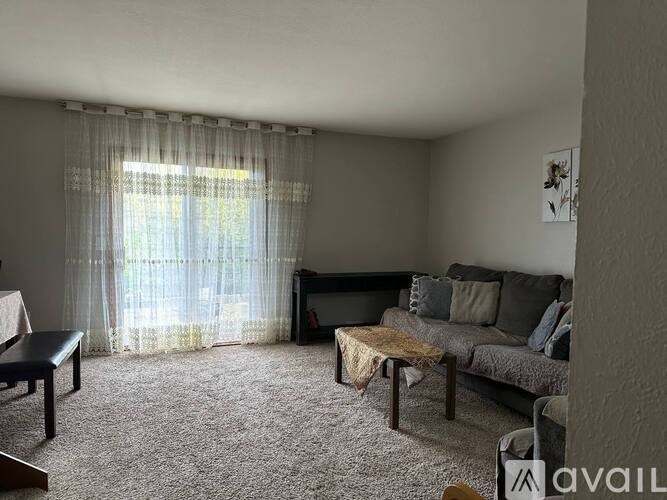 A living room with a grey couch, a coffee table, and a window with curtains.