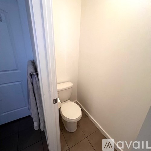 A toilet in a small bathroom with a towel hanging on the door.