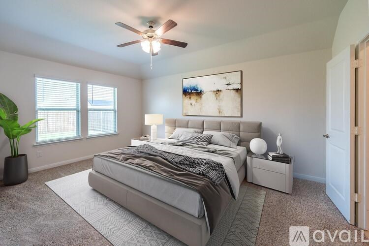 A bedroom with a large bed, a ceiling fan, and a painting on the wall.