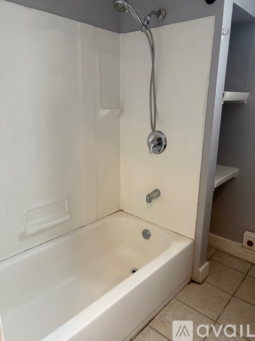 A white bathtub with a shower head attached to the wall.