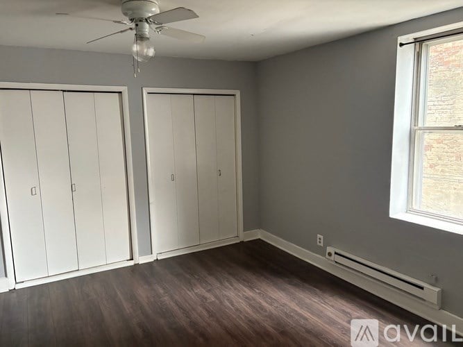 A room with a ceiling fan and a window with a view of a brick building outside.