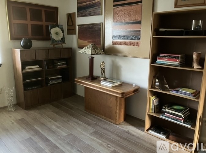 A room with a bookshelf, a table with a lamp, and a painting on the wall.