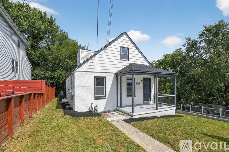 A small white house with a grey roof is surrounded by a fence and greenery.