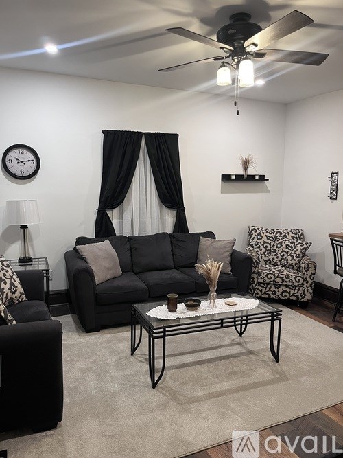 A living room with a black couch, a glass coffee table, and a ceiling fan.