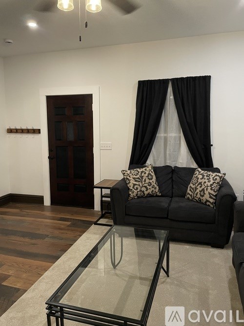 A living room with a black couch and a glass coffee table.