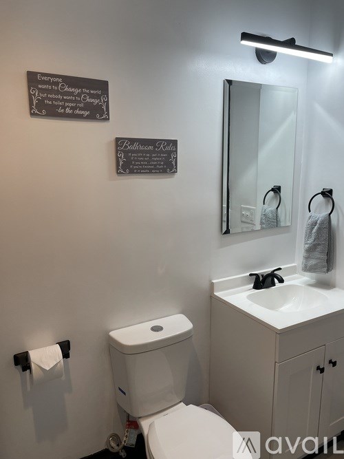 A bathroom with a toilet, sink, mirror, and two signs on the wall.