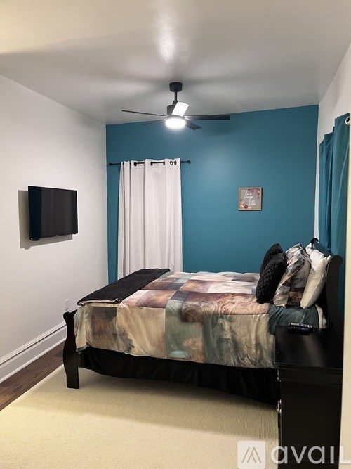 A bedroom with a bed, a ceiling fan, and a flat-screen TV mounted on the wall.