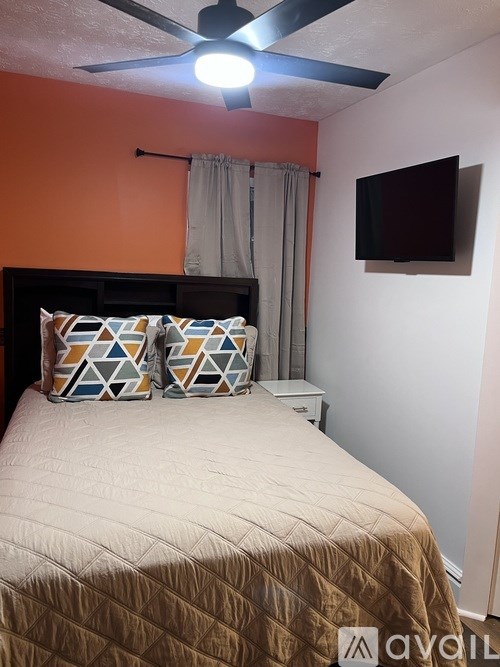 A bedroom with a bed, a ceiling fan, and a flat screen TV mounted on the wall.