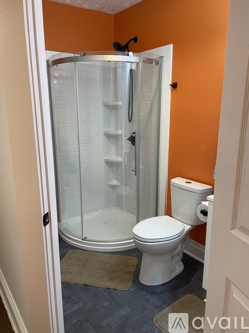 A bathroom with orange walls has a white toilet and a walk-in shower.