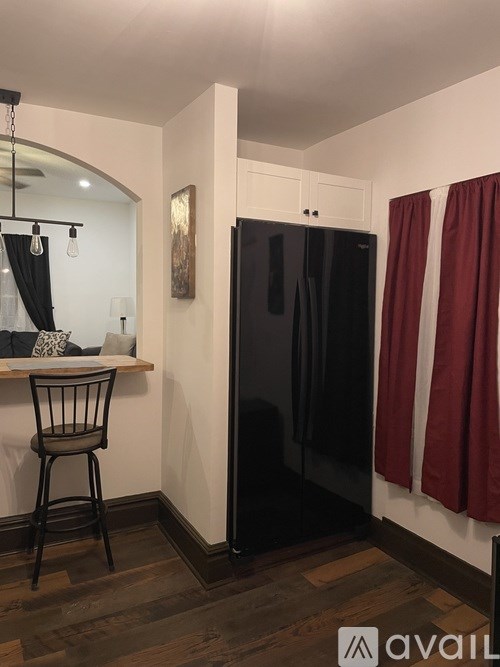 A black refrigerator is in a kitchen with a wooden table and a chair.