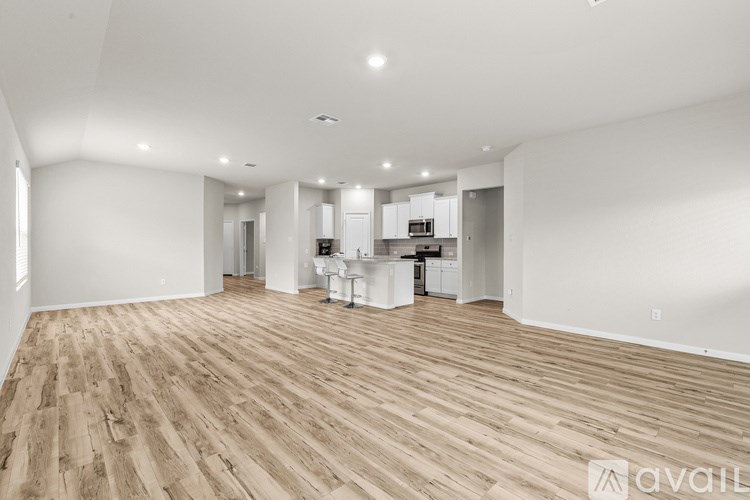 A spacious room with wooden flooring and a kitchen area in the background.