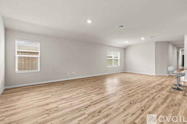 A spacious room with wooden flooring and two windows.