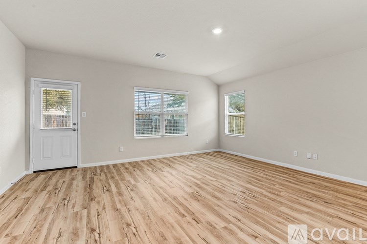 A room with wooden flooring and white walls, with a door and two windows.