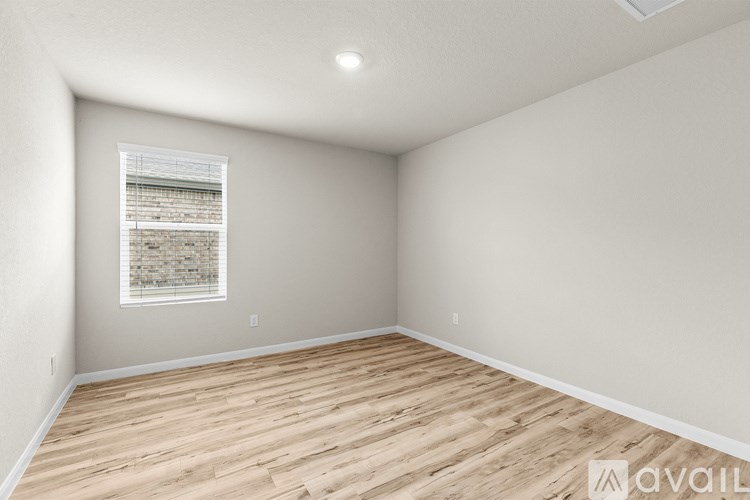A room with wooden flooring and a window showing a brick wall outside.