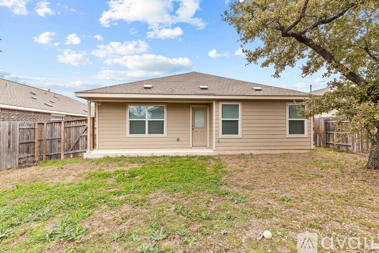 A house with a brown roof and tan siding is surrounded by a fence and a tree.