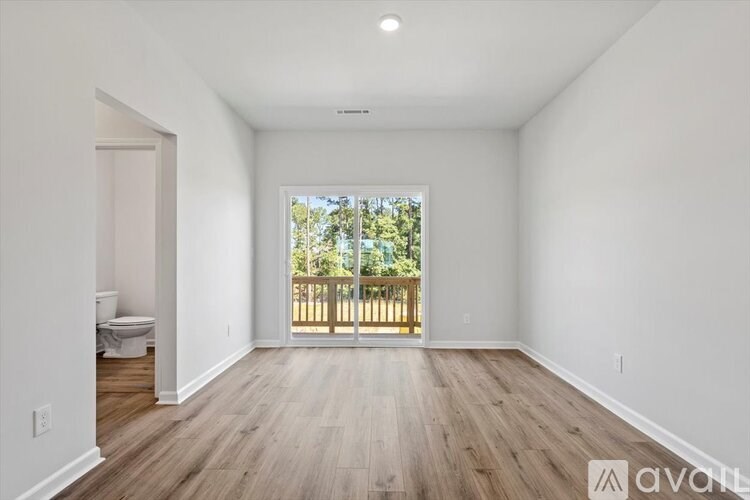 A spacious room with wooden floors and a large window overlooking a deck.