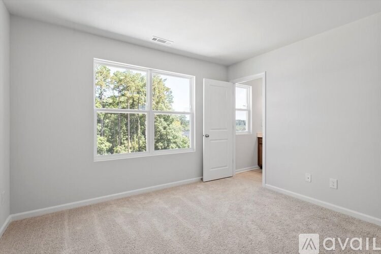 A room with a carpeted floor, a door, and a window with a view of trees outside.