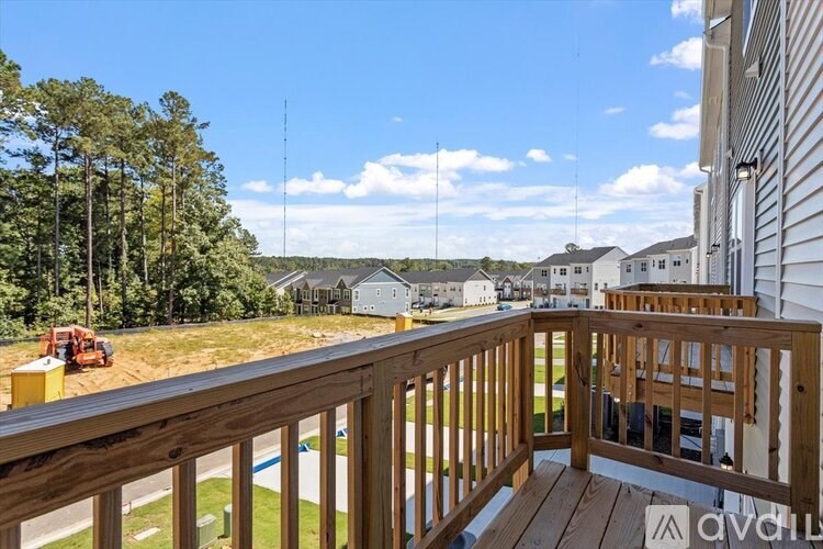 A wooden deck overlooks a grassy area with a house and trees in the distance.