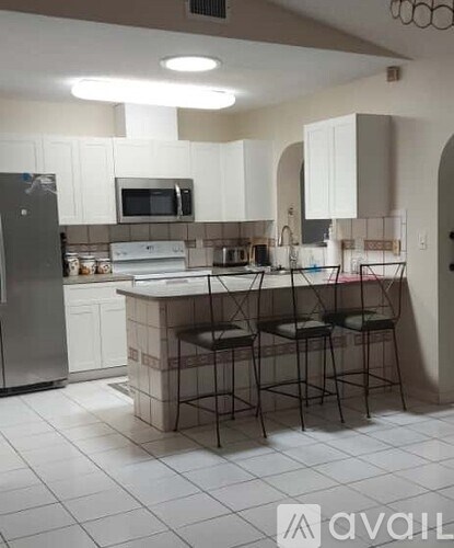 A kitchen with white cabinets and a white island with three stools.