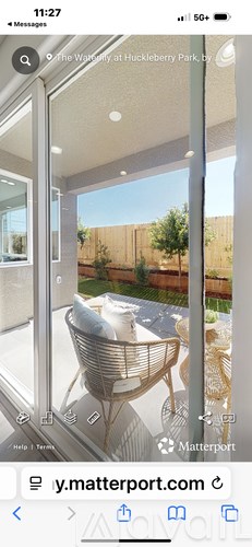 A modern glass table with a woven basket on top is in the foreground of a bright outdoor patio area.